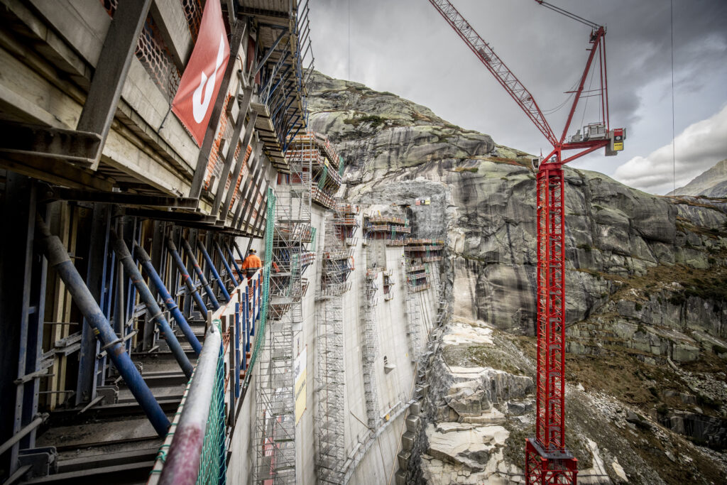 Blick vom Gerüst der neuen Staumauer auf die andere Seite der Mauer. Ebenfalls im Bild ein grosser, roter Kran.